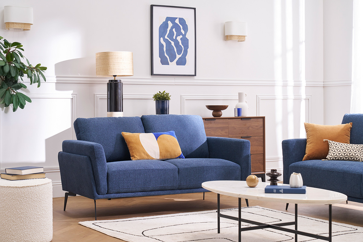 Design-Zweisitzer-Sofa aus blauem Stoff in einem hellen Wohnzimmer mit Couchtisch und moderner Dekoration.