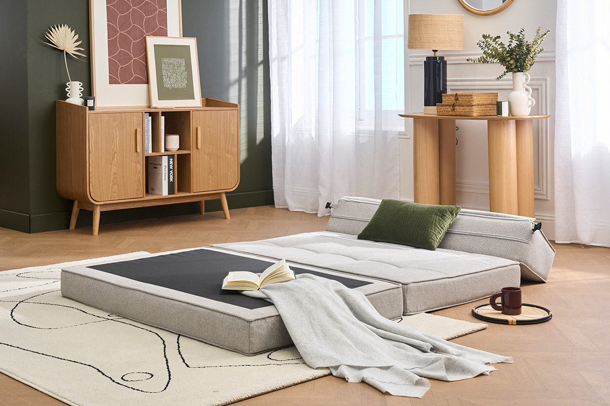 2-Sitzer KATY Schlafsessel ausgeklappt als Bett, hellgrauer Stoff, gr�nes Kissen, in einem modernen Wohnzimmer.