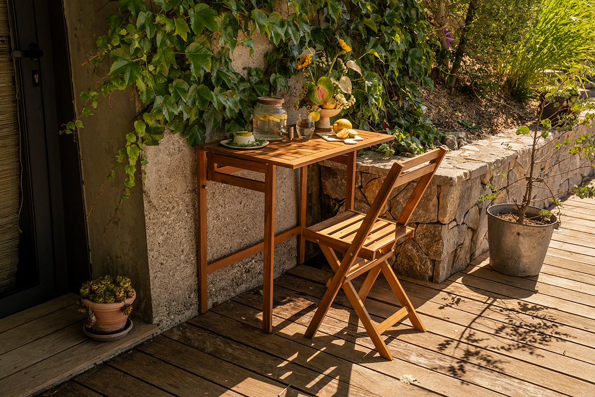 Klappbarer Balkon Tisch aus Massivholz, L80 cm, 3/4-Ansicht mit Stuhl und Dekorationen auf einem Balkon