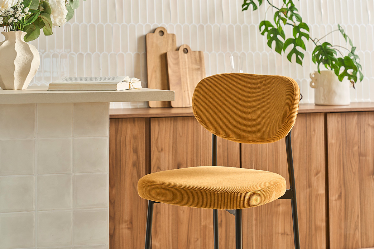 Fester Barhocker aus senfgelbem Cordvelours, Seitenansicht, mit Hintergrunddekoration.