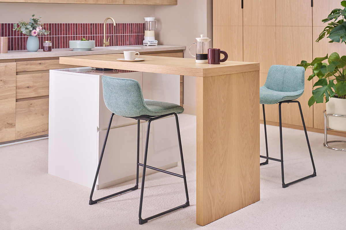 Barhocker aus celadongr�nem Stoff und schwarzem Metall um eine Theke aus hellem Holz.