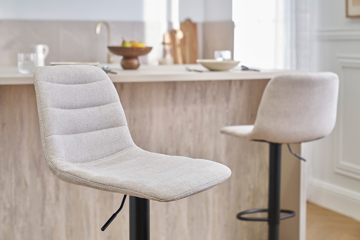 Verstellbare Barhocker aus beigefarbenem Stoff und schwarzem Metall vor einer Theke.