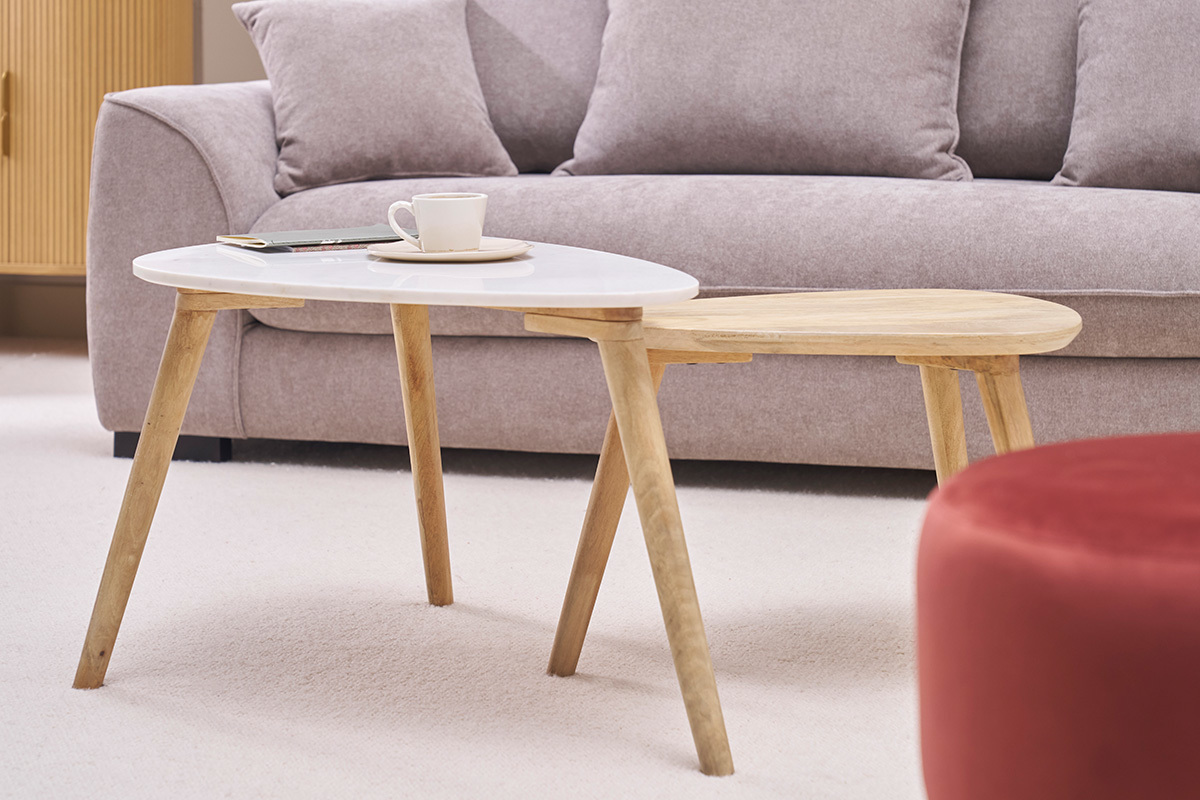 Verschachtelte Couchtische aus wei�em Marmor und Mangoholz vor einem Sofa.