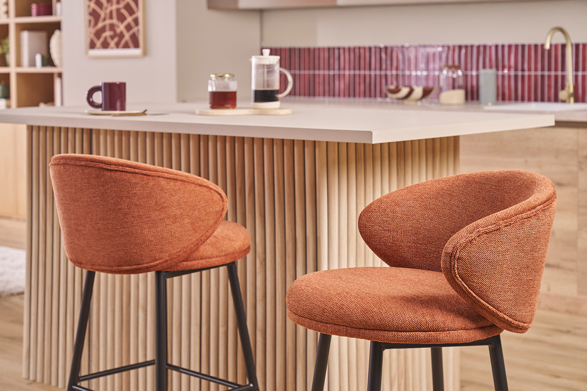 Zwei Barhocker aus verbrannter Erde Stoff mit schwarzen Metallbeinen vor einer K�cheninsel.