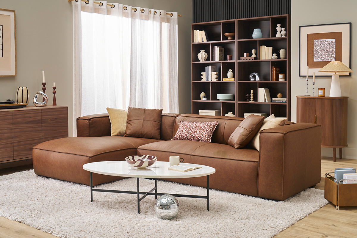 Wohnzimmer mit dunklem Holzbcherregal mit 12 Fchern, braunem Sofa, weiem Couchtisch und dekorativem Rahmen.