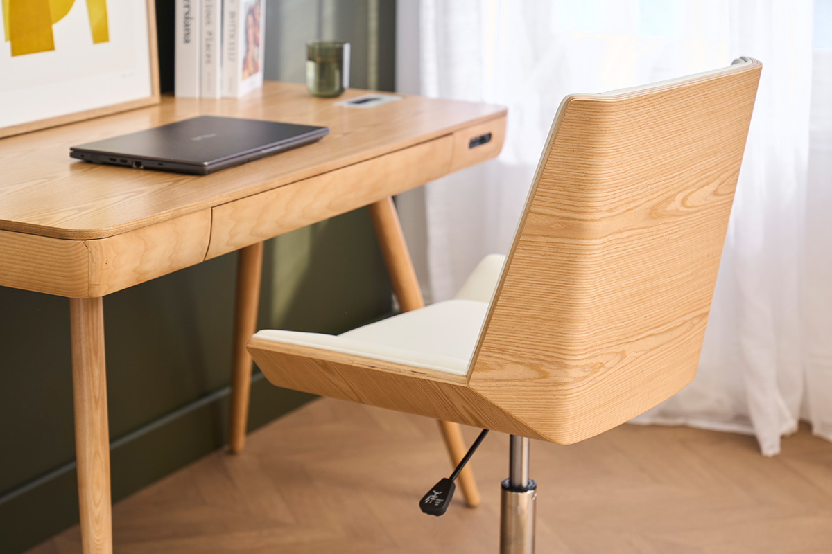 B�rostuhl MELKIOR mit Rollen, helles Holz und wei�er Sitz, neben einem Holzschreibtisch.