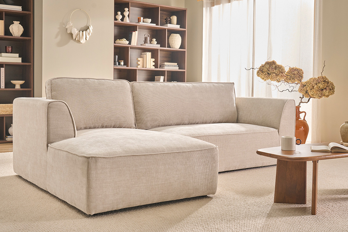 Ecksofa links in beige Stoff mit Couchtisch in einem hellen Wohnzimmer.