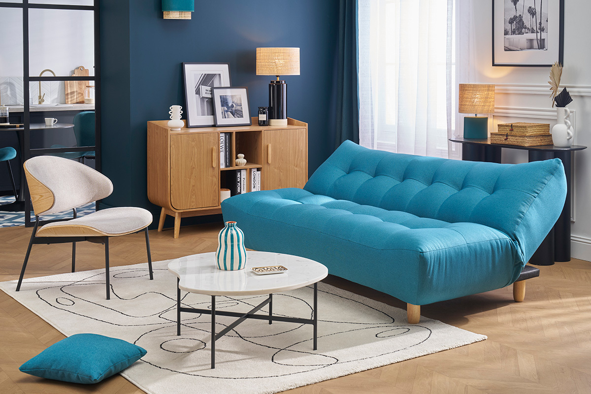 Blaues Entenblau Schlafsofa YUMI mit hellen Holzbeinen in einem modernen Wohnzimmer.