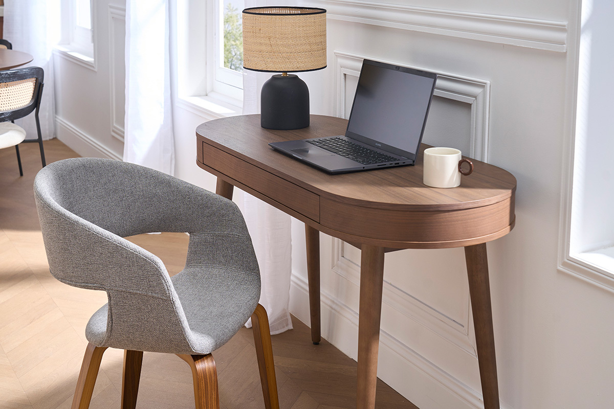 Designerstuhl aus grauem Stoff mit dunklen Holzbeinen, Seitenansicht neben einem Schreibtisch.