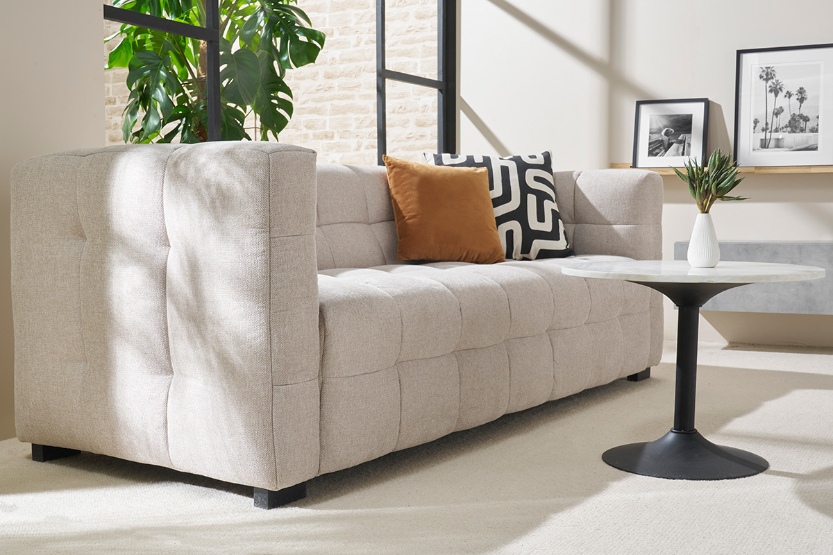 Beige Dreisitzer-Sofa mit Kissen und runder Couchtisch in hellem Wohnzimmer.