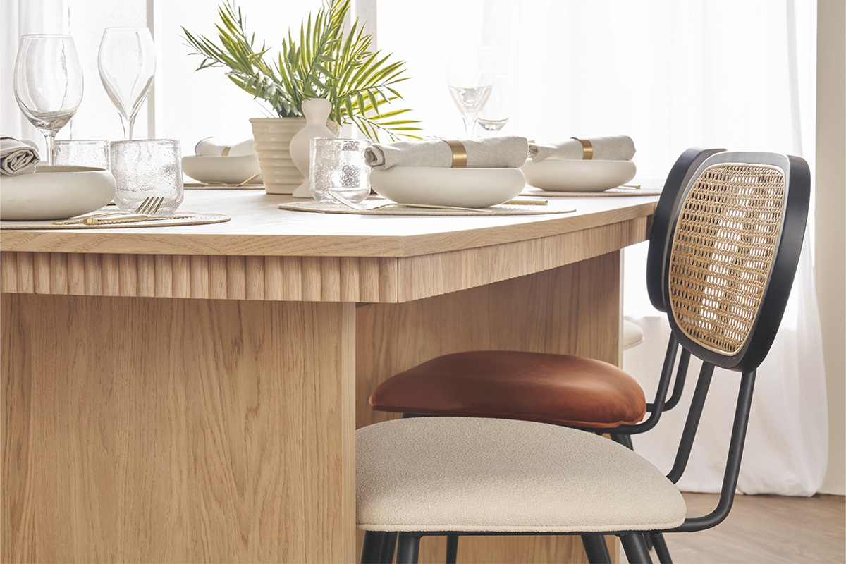 Zwei SWANN Designst�hle aus wei�em Boucl�-Stoff und Rattan, vor einem Tisch aus hellem Holz.