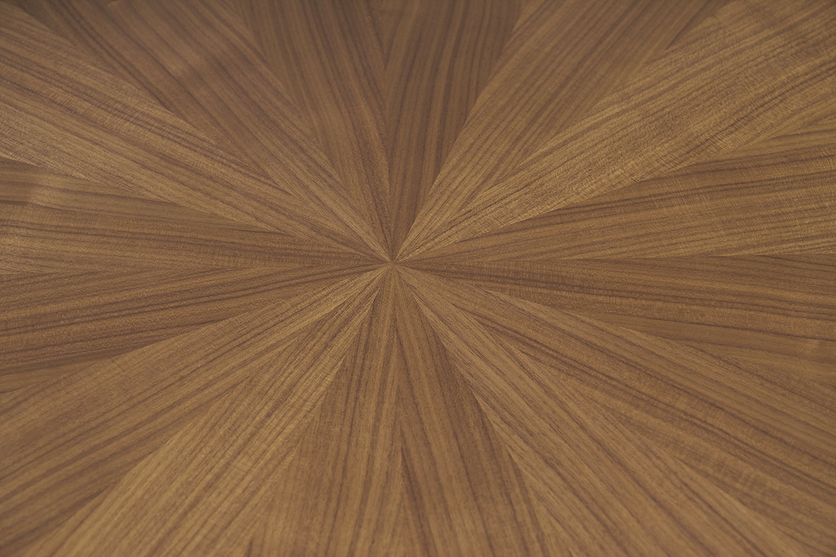 Runder Tischplatte mit Nussbaumfurnier in Sonnenmuster aus der Nhe betrachtet.