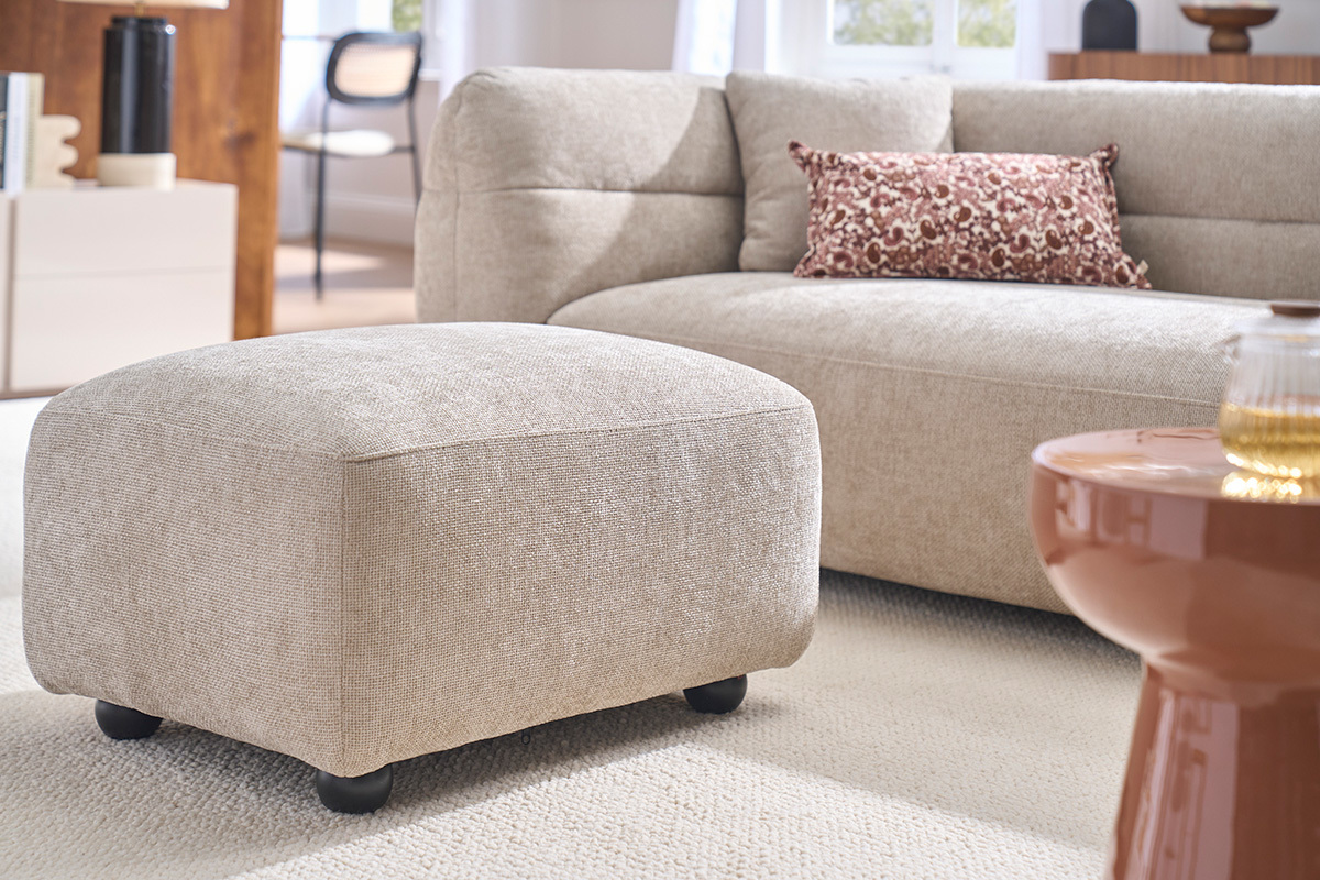 Beiger Stoffhocker als Fu�ablage, mit Sofa im Hintergrund, 3/4-Ansicht