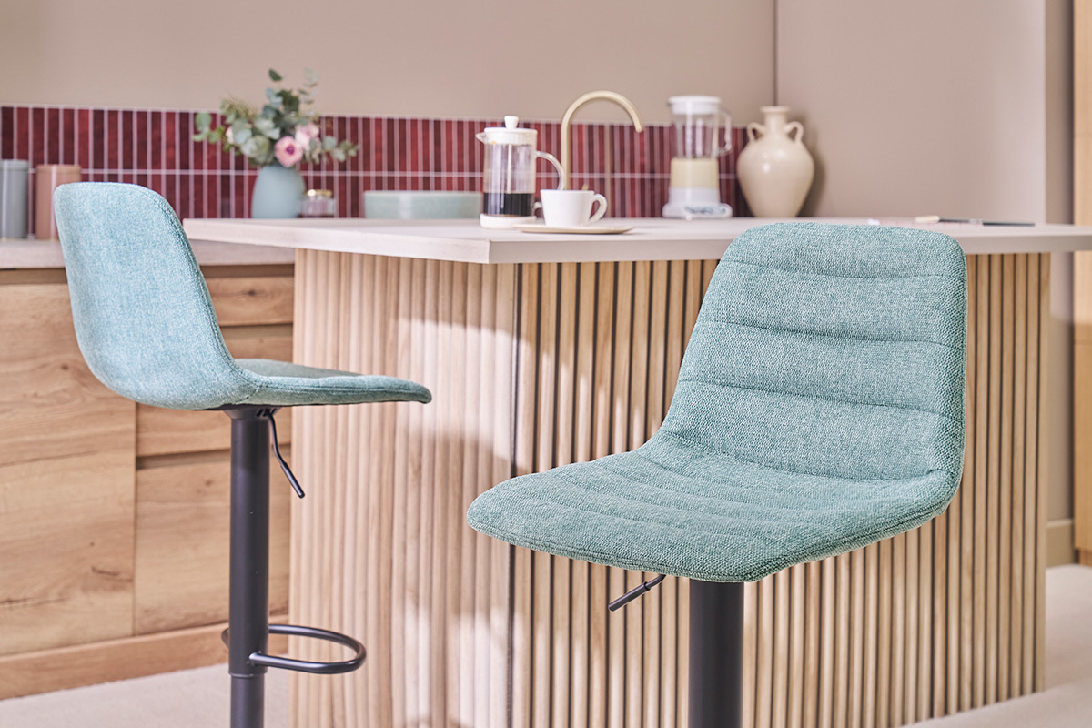 Zwei Barhocker aus Celadon-Stoff vor einer Holztheke.