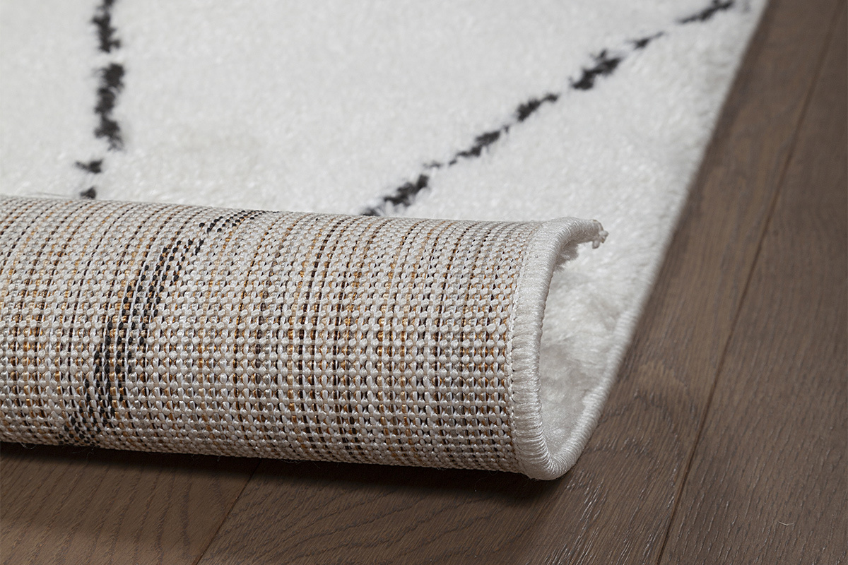 Nahaufnahme des SILAN-Teppichs mit schwarzen Mustern und Stofftextur, teilweise gerollt.