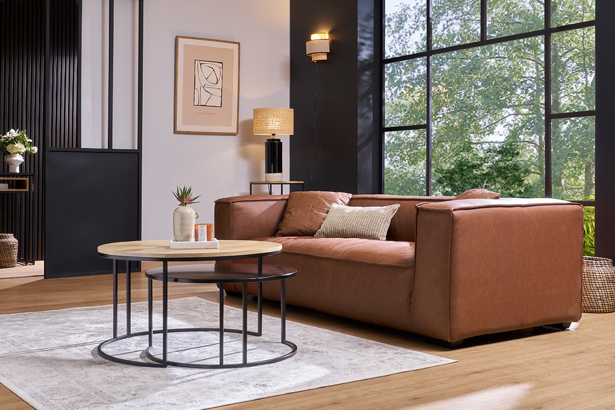 Zwei runde, ineinander schiebbare Couchtische aus Mangoholz und schwarzem Metall, vor einem Sofa platziert.