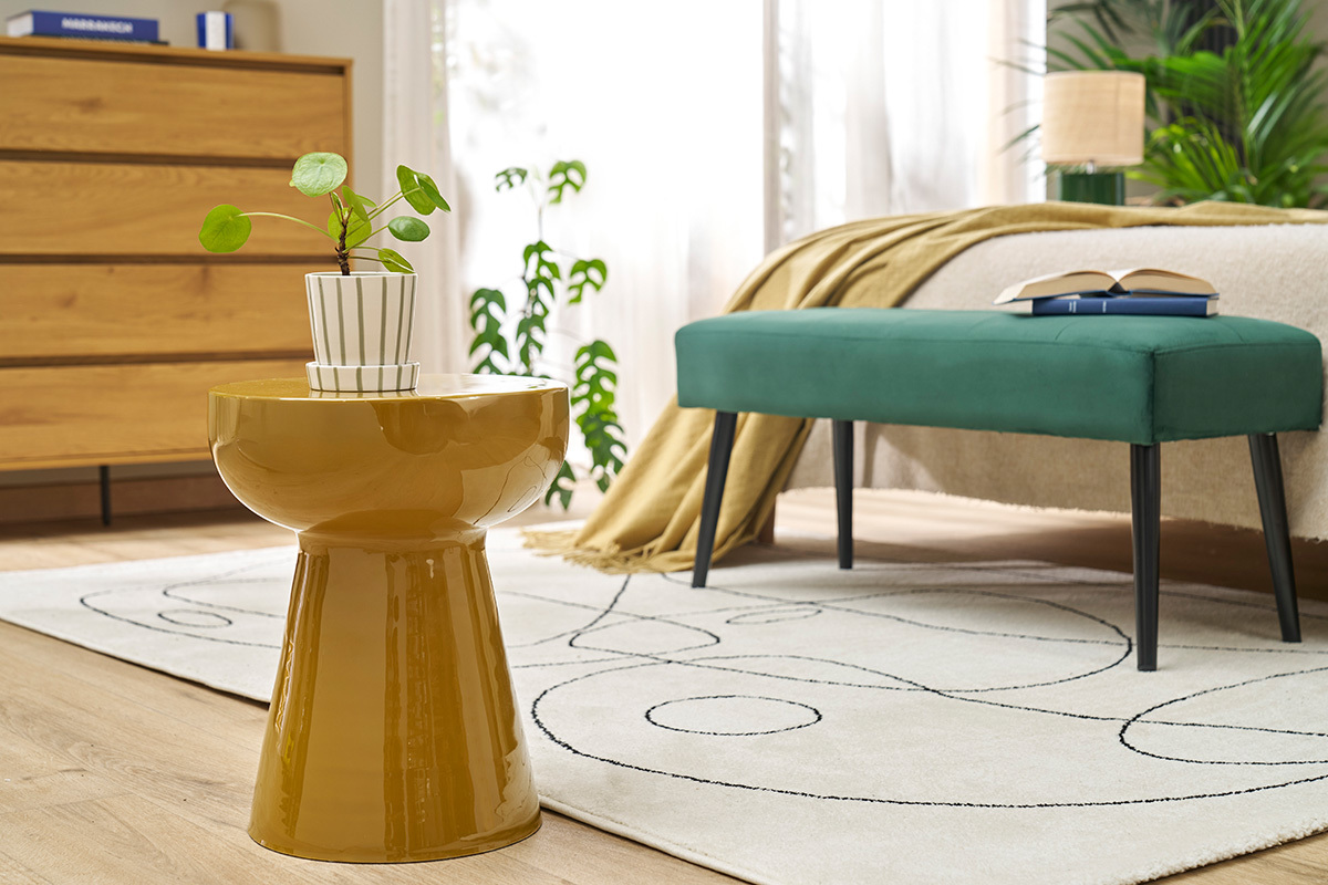 Runder Beistelltisch aus bronzefarbenem emailliertem Metall mit einer Pflanze von vorne betrachtet in einem Schlafzimmer.