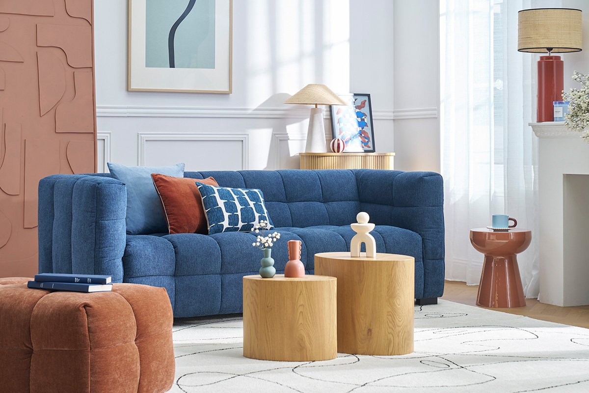 Wohnzimmer mit blauem Sofa, bunten Kissen, terrakottafarbener runder Beistelltisch rechts.