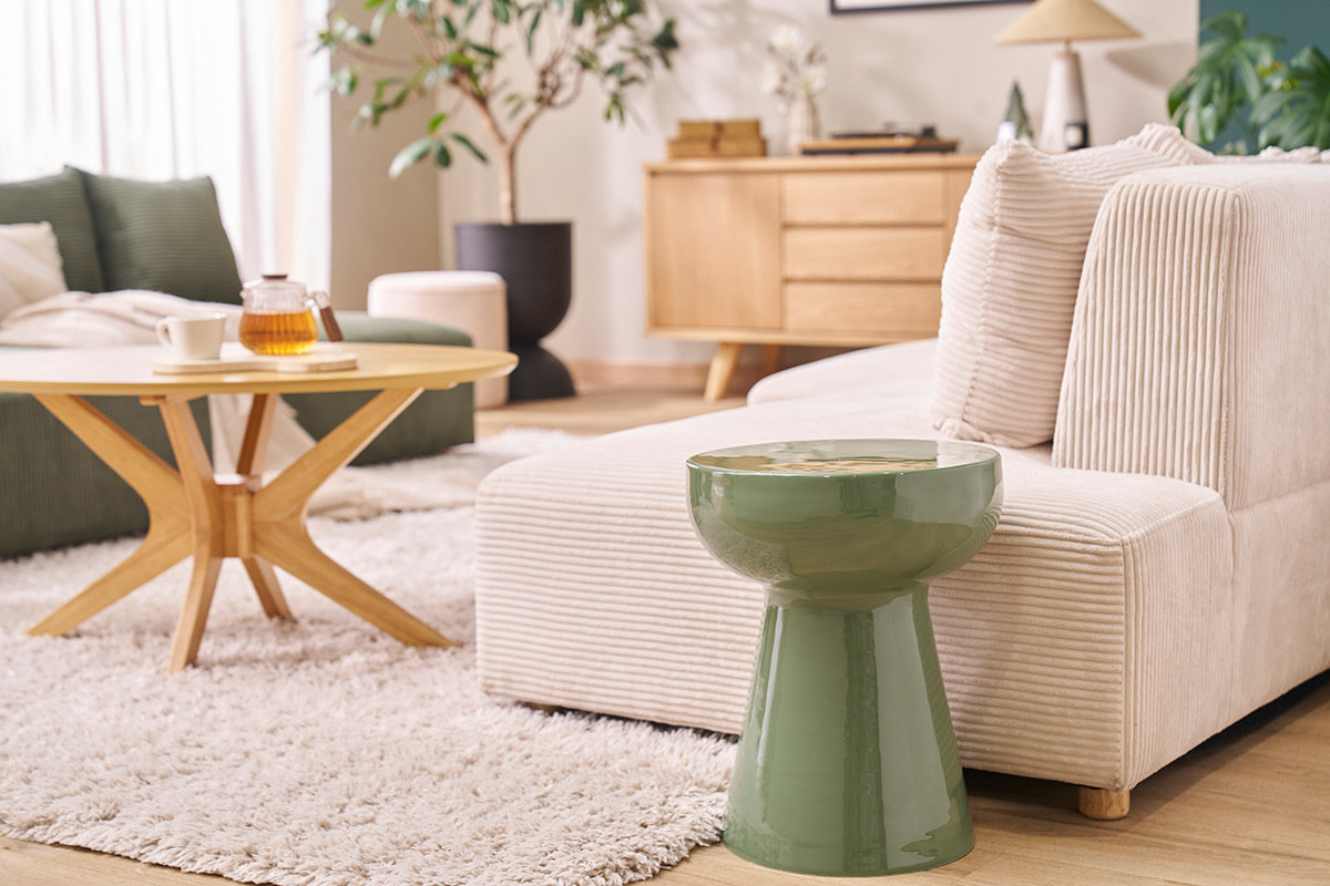 Runder Beistelltisch aus kaki-gr�nem emaillierten Metall neben einem beigen Sofa, gezoomte Ansicht.