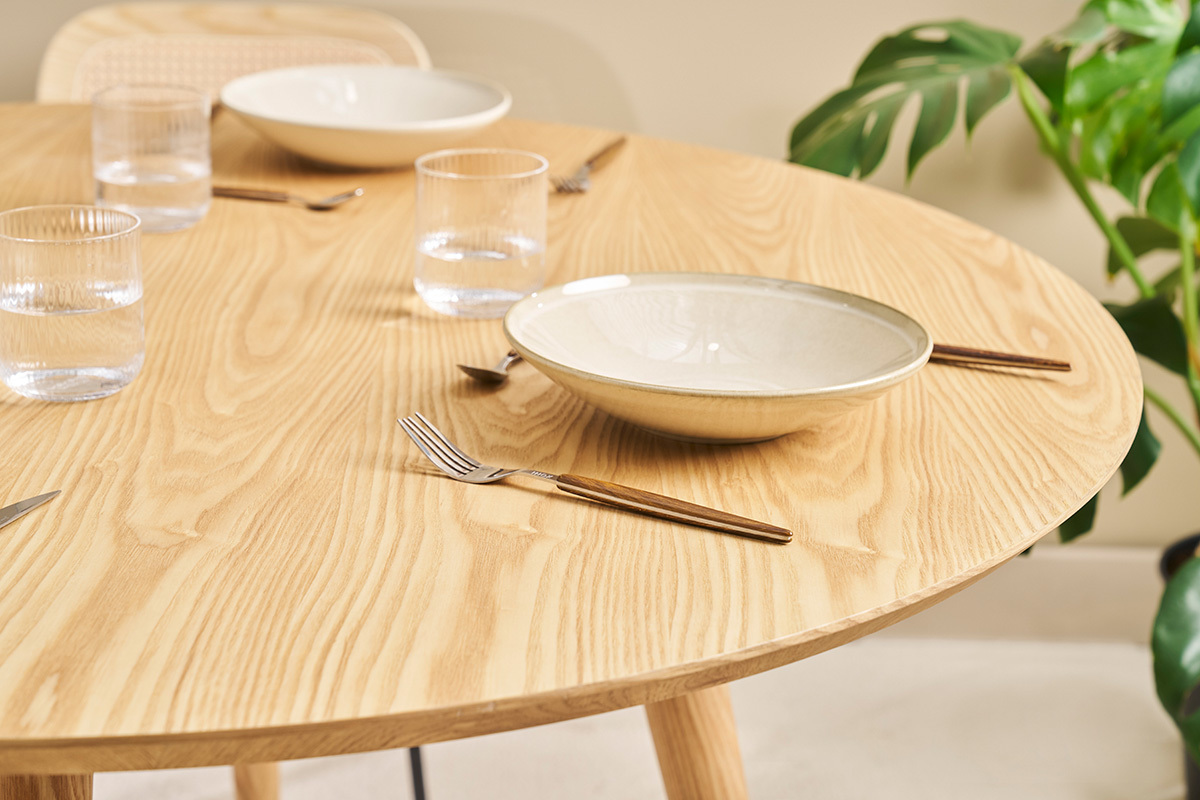 Runder Tisch aus hellem Eichenholz D120 cm mit Geschirr und Besteck, Draufsicht.