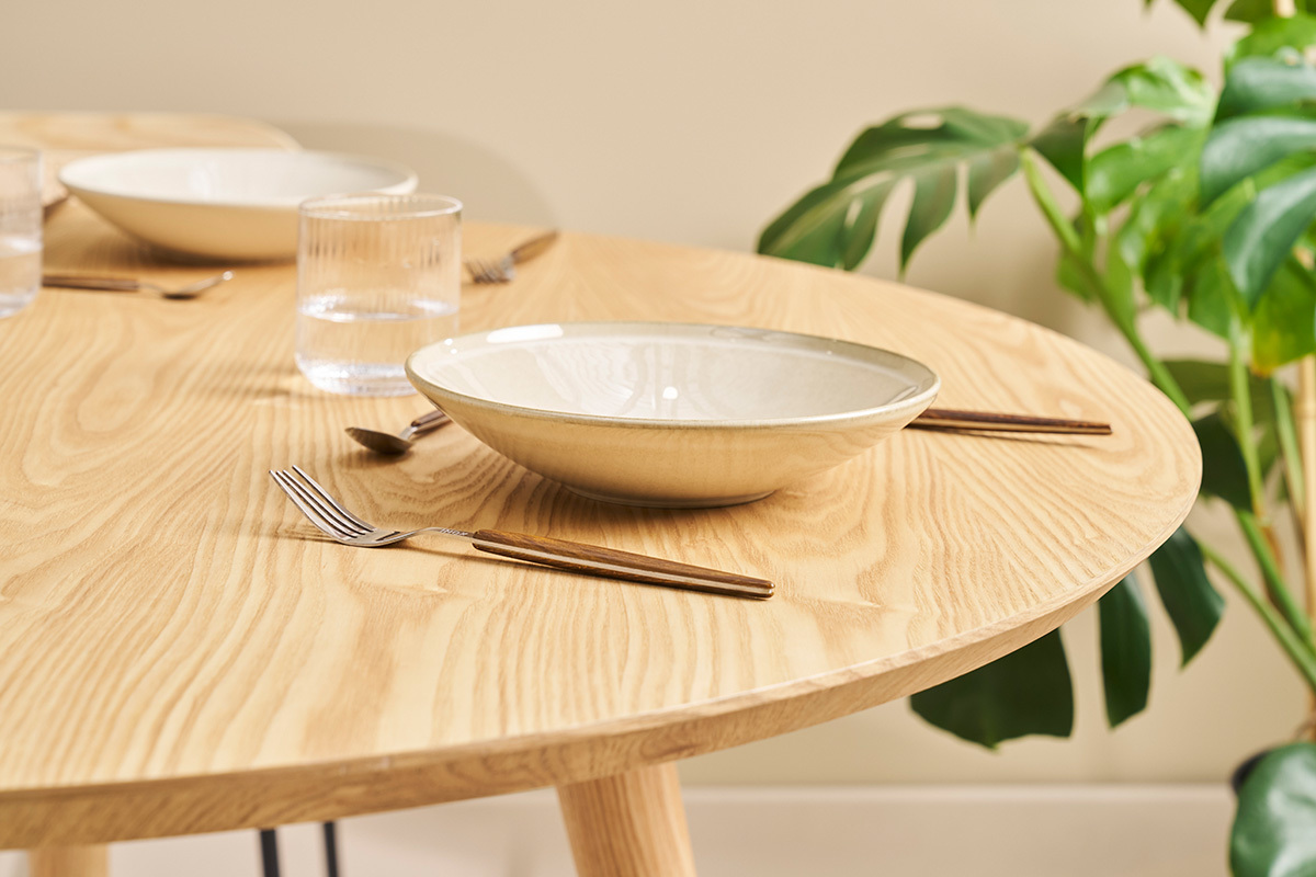 Runder Eichentisch mit Besteck und Teller, Nahaufnahme.