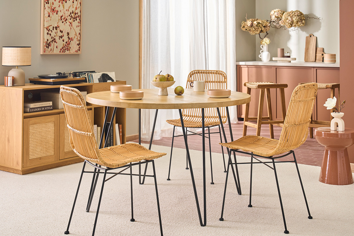Runder Holztisch mit Metallbeinen, umgeben von Korbst�hlen, in einem modernen Interieur.