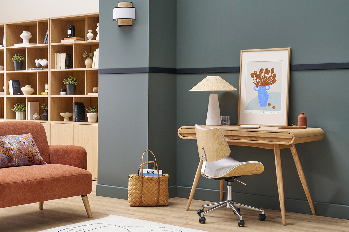 Skandinavischer Schreibtisch aus hellem Holz mit Lampe und Stuhl vor einer grauen Wand.