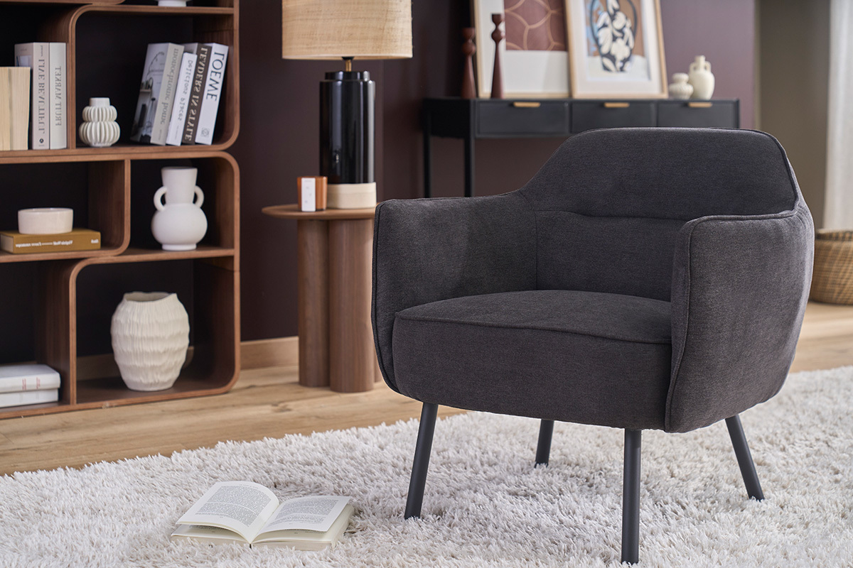 Design-Sessel LAURENS aus dunkelgrauem Samtstoff, in Dreiviertelansicht mit Innenraumdekoration.