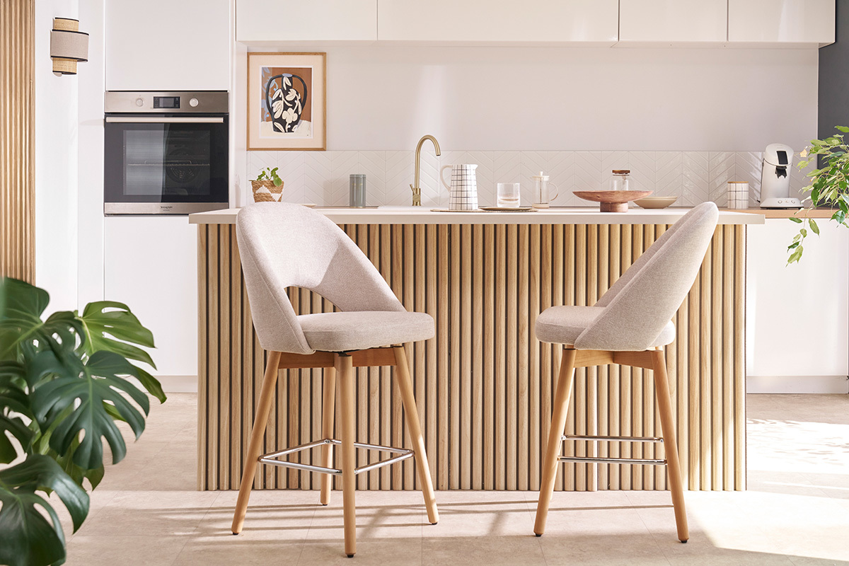 Beige Stoff-Barhocker mit massiven Hevea-F��en vor einer K�chentheke.