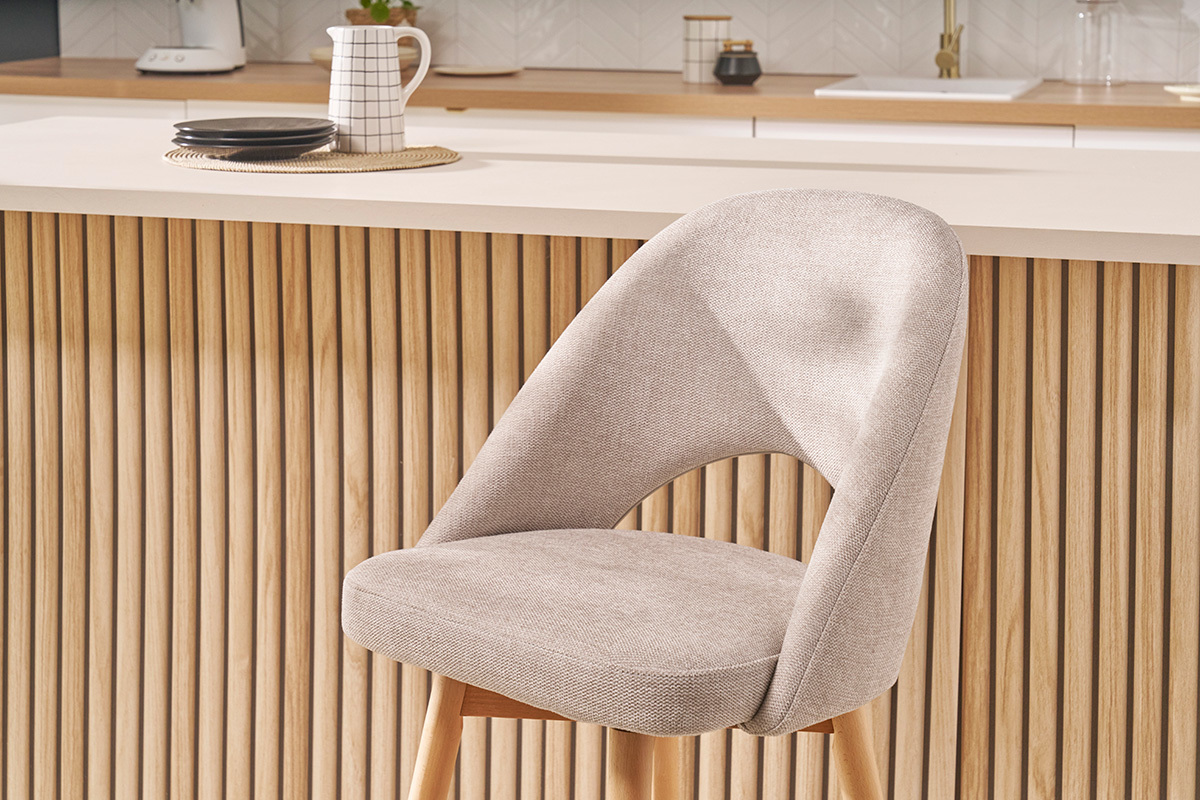 Skandinavischer Barhocker aus beigem Stoff und massivem Gummibaumholz vor einer Holztheke.