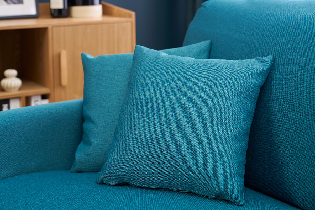 Kissen des wandelbaren blauen Samtsofas SKANDY in Nahaufnahme neben einem Holzmbel.