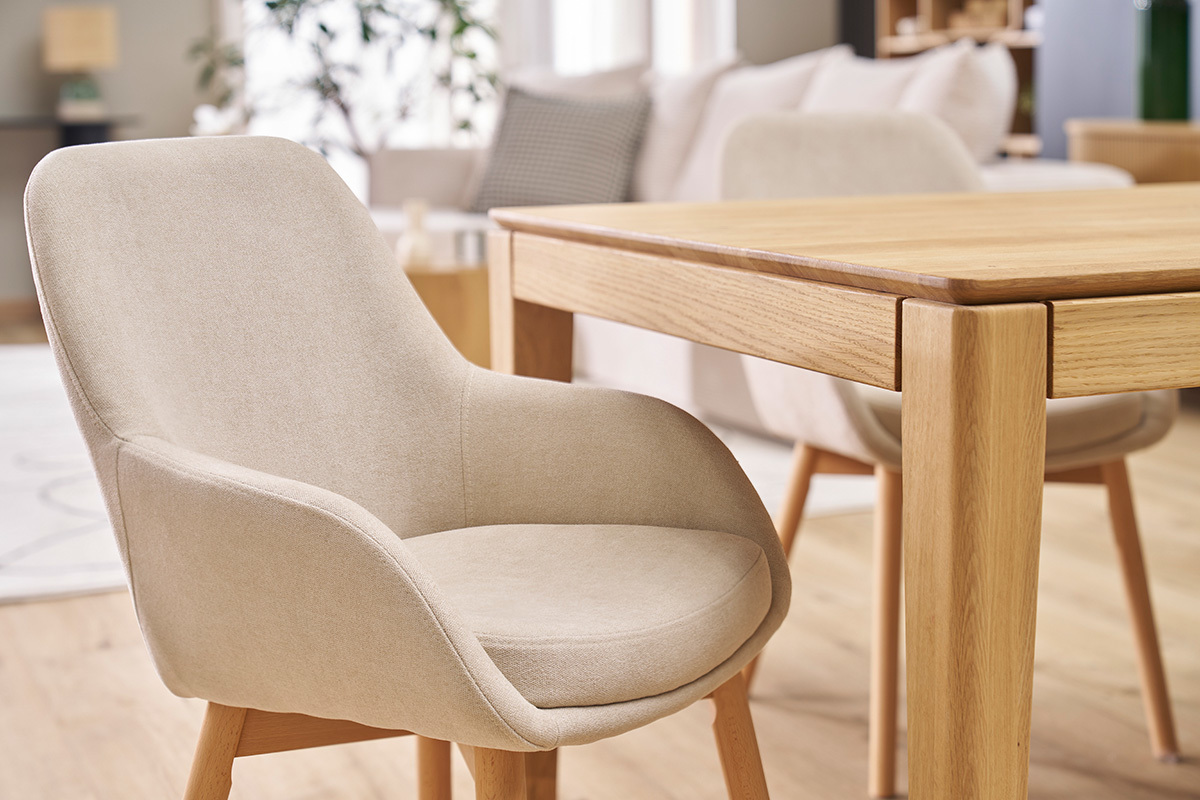 Skandinavischer Sessel aus beigem Stoff und hellem Holz, Seitenansicht, neben einem Holztisch.