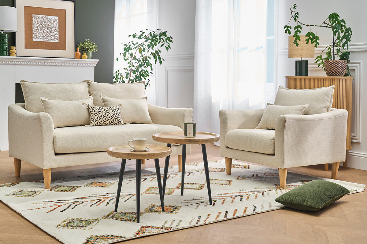 Skandinavischer Sessel beige KATE mit Kissen, umgeben von Couchtischen, Gesamtansicht in einem Wohnzimmer