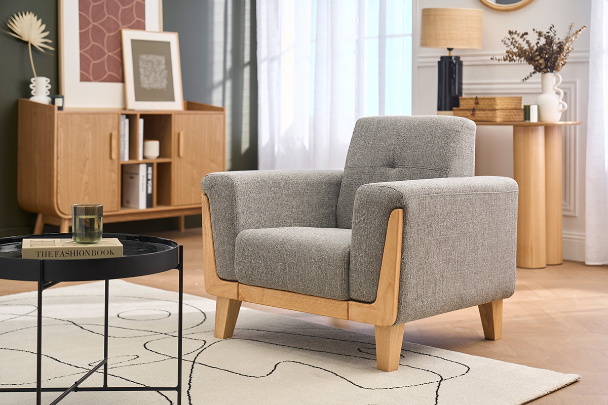 Skandinavischer Sessel aus grauem Stoff und hellem Holz, Ansicht von 3/4, mit Couchtisch und Sideboard im Hintergrund.