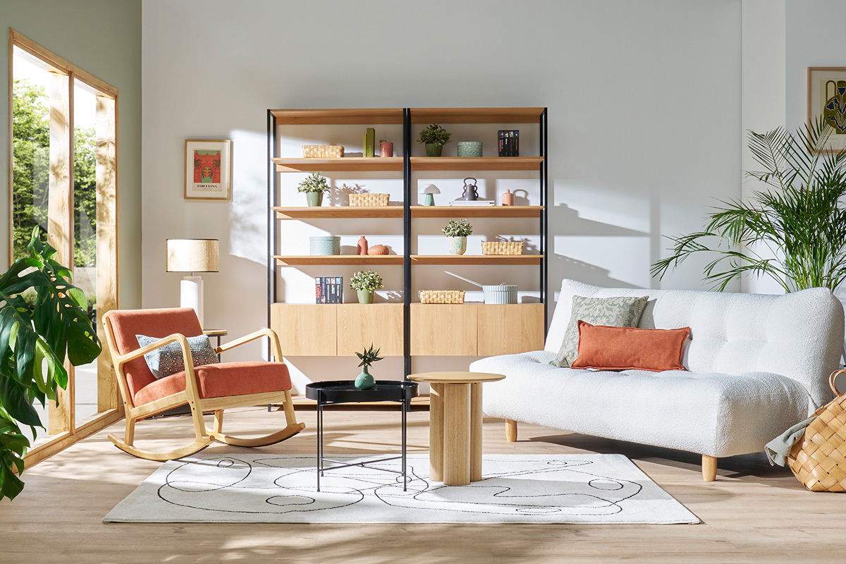 Schlafsofa YUMI in modernem Wohnzimmer mit Sessel und Regalen, Frontansicht.