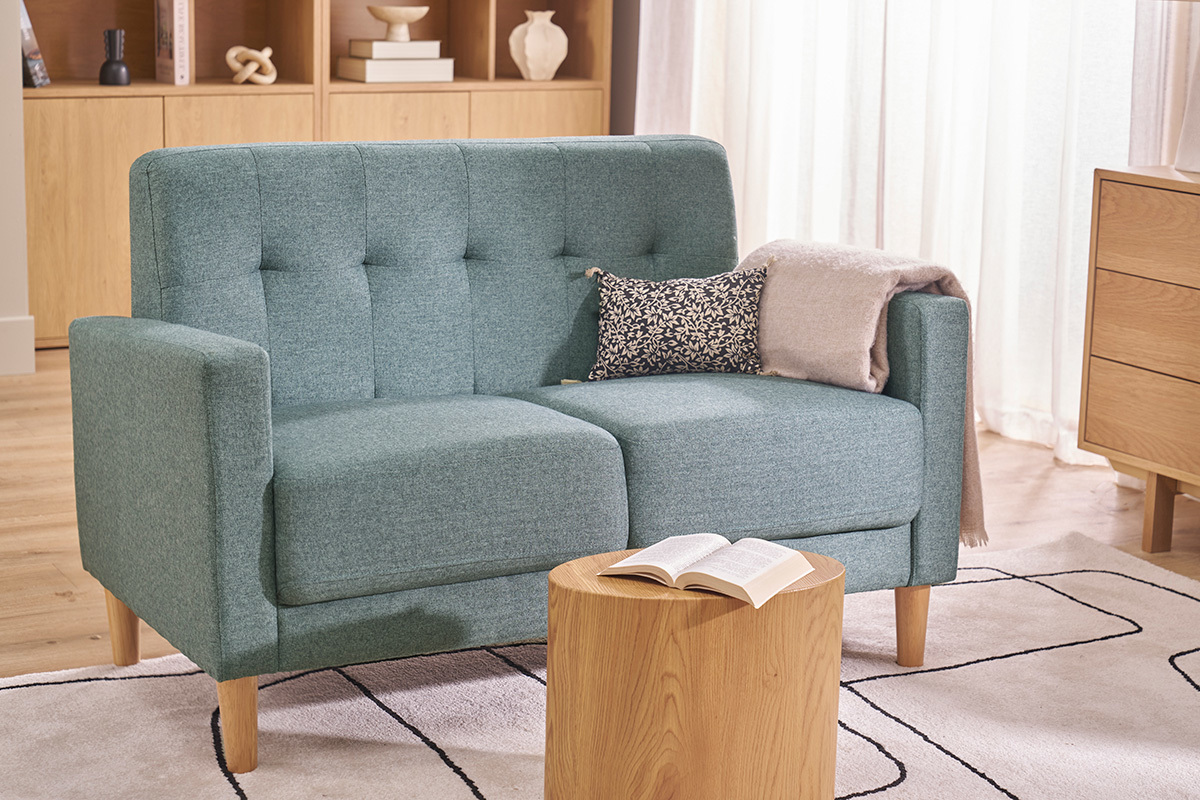 Skandinavisches 2-Sitzer Sofa in Graugr�n aus Stoff und hellem Holz, Frontansicht mit Kissen und Plaid.