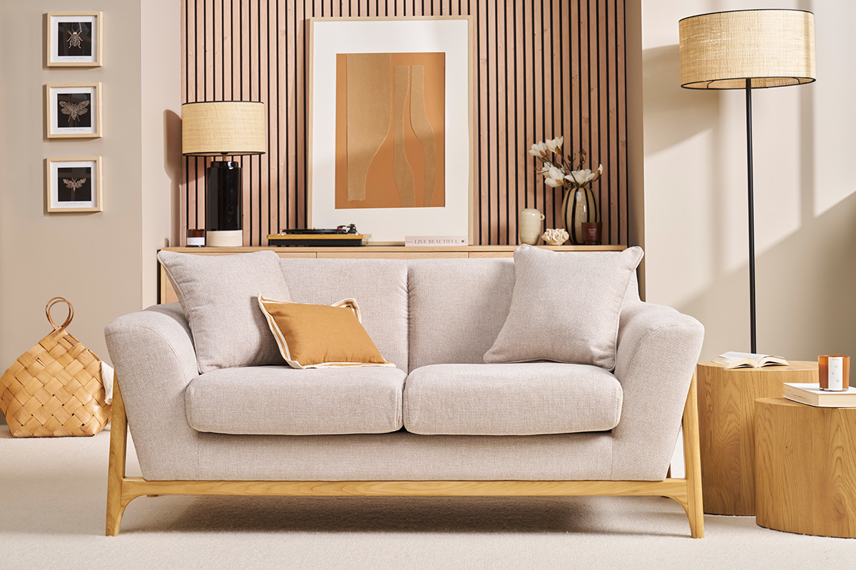 Beige Samtstoff 2-Sitzer Sofa mit hellen Holzbeinen, Frontansicht in einem dekorierten Wohnzimmer.
