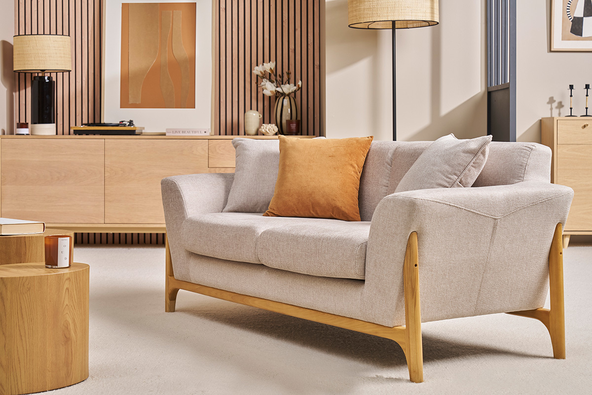 Beige Zweisitzer-Sofa aus Stoff und hellem Holz, Winkelsicht, mit orangefarbenem Kissen.