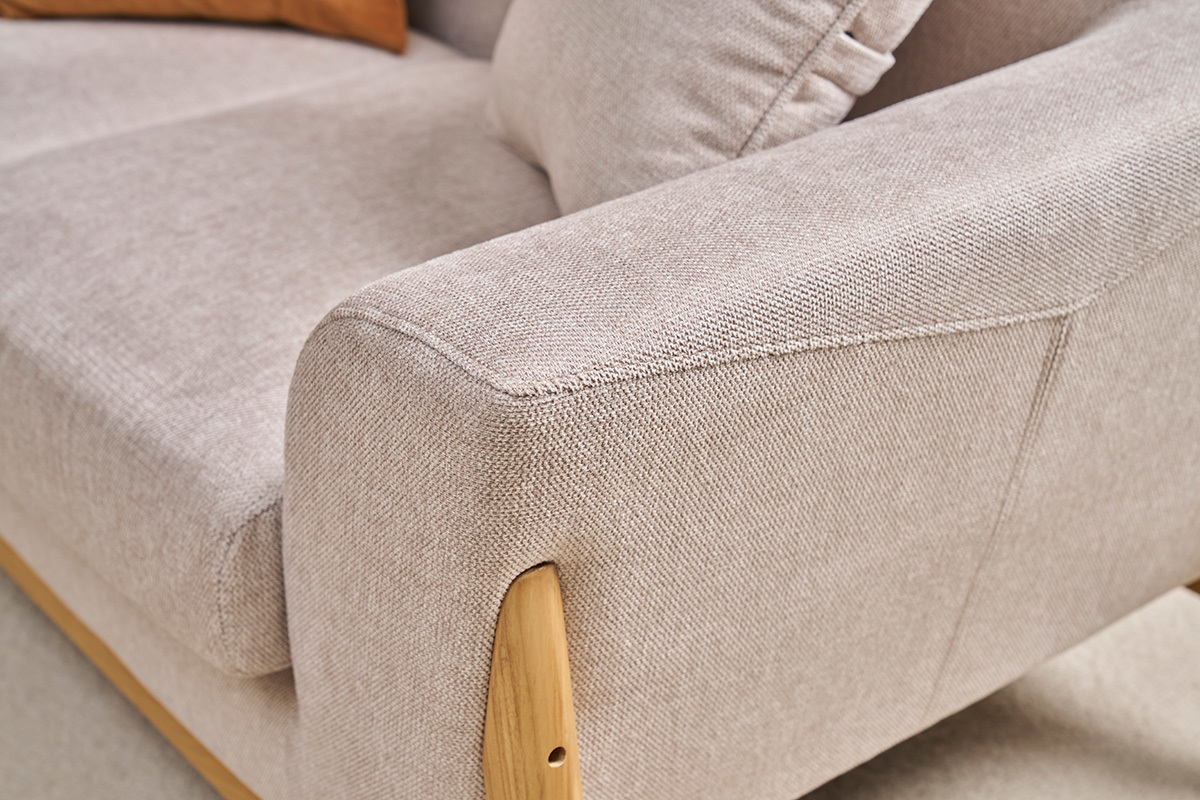 Detail eines skandinavischen Sofas aus Stoff in Samtoptik, beige und hellem Holz.