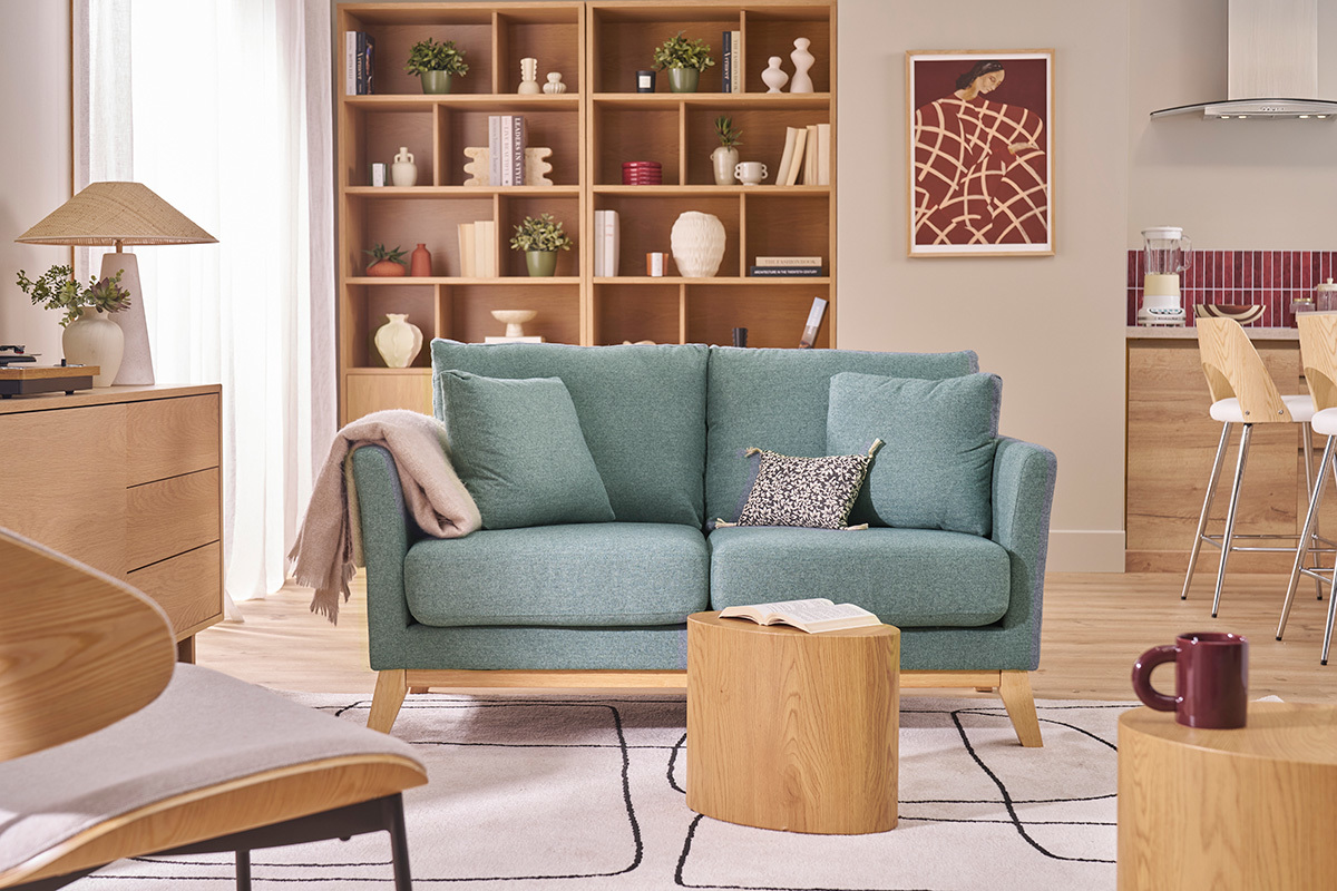 Zweisitzer-Sofa aus graugr�nem Stoff und hellem Holz mit Kissen, Frontansicht in einem Wohnzimmer.