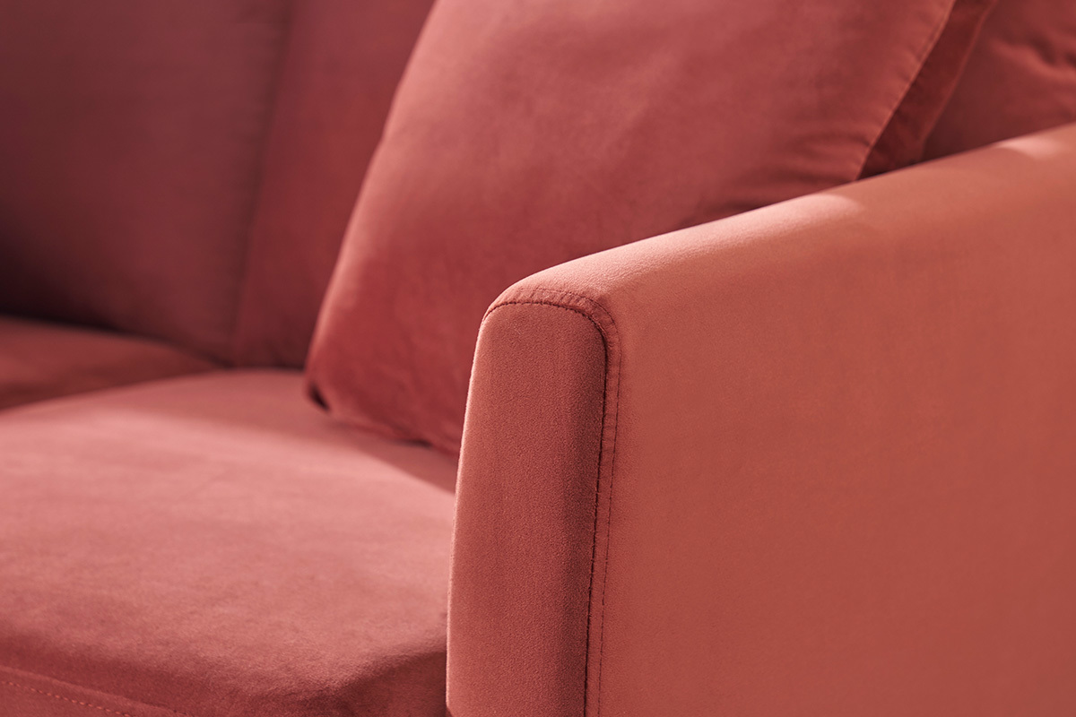 Nahaufnahme eines skandinavischen Sofas in Terrakotta-rotem Samt mit sichtbarem Armlehne und Kissen.