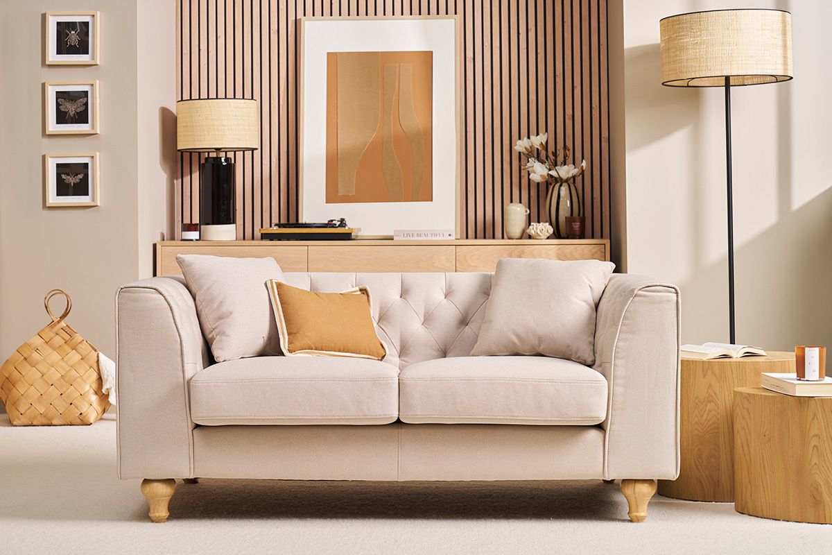 Beige Zweisitzer-Sofa mit Knopfheftung und Kissen, Frontansicht.