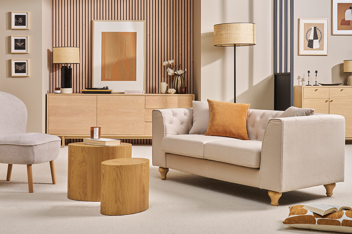 Beige MONTAIGNE 2-Sitzer Sofa mit Stoffbezug, Seitenansicht mit orangefarbenem Kissen, in einem eleganten Wohnzimmer.