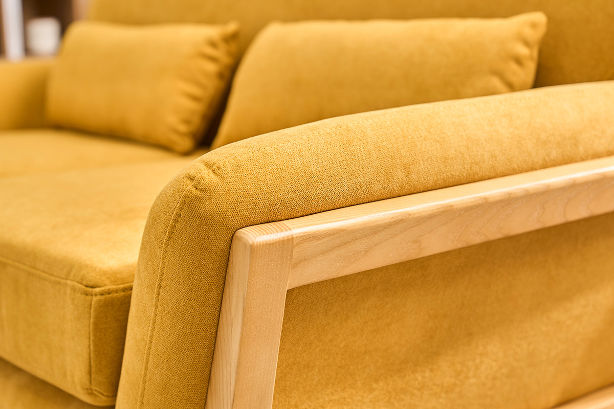 Detail eines skandinavischen 2-Sitzer-Sofas aus Senfgelbem Stoff mit Armlehne aus hellem Holz.