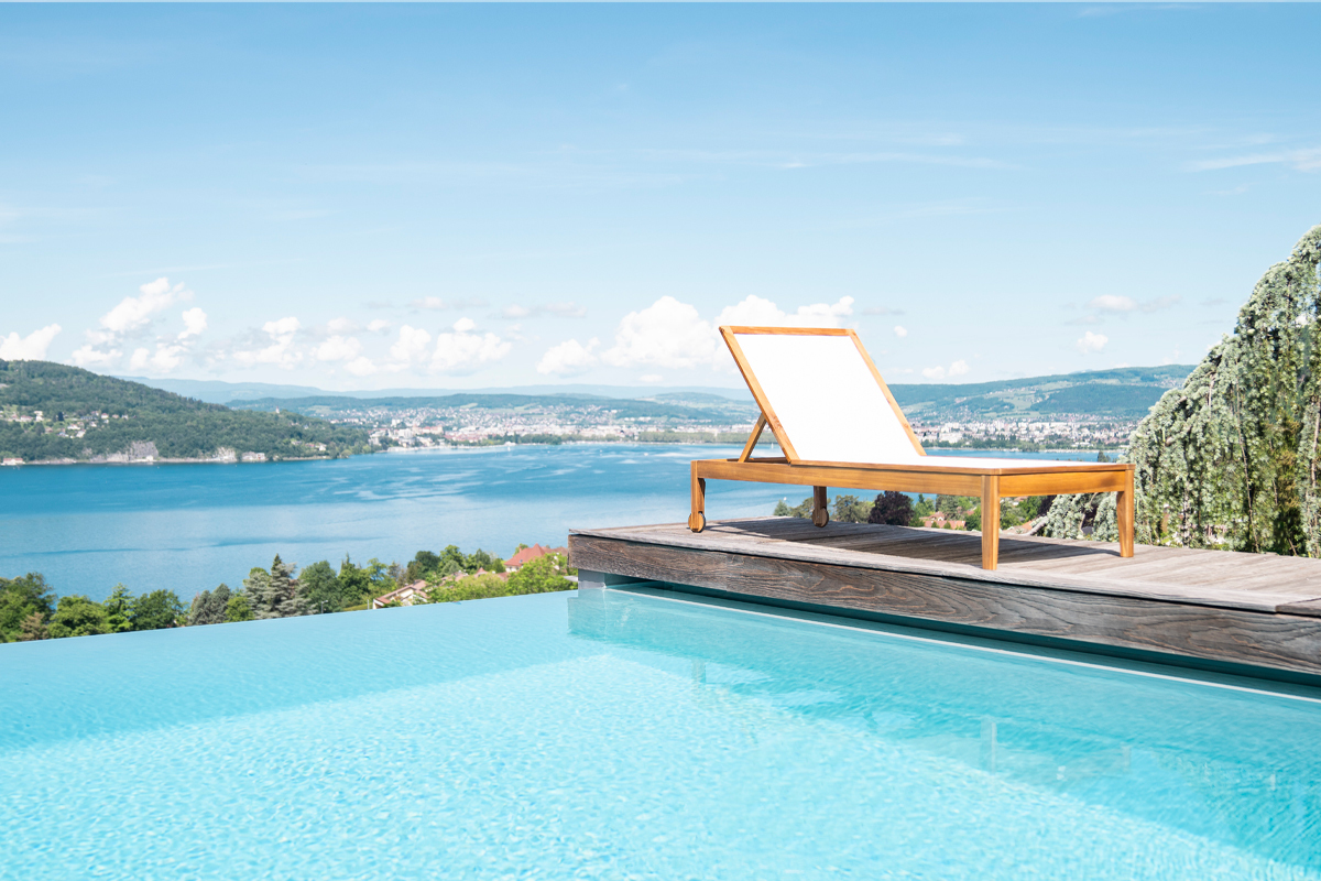 Wei�es Sonnenbad und Massivholz NAVEEN neben einem Pool mit Seeblick und Bergen.