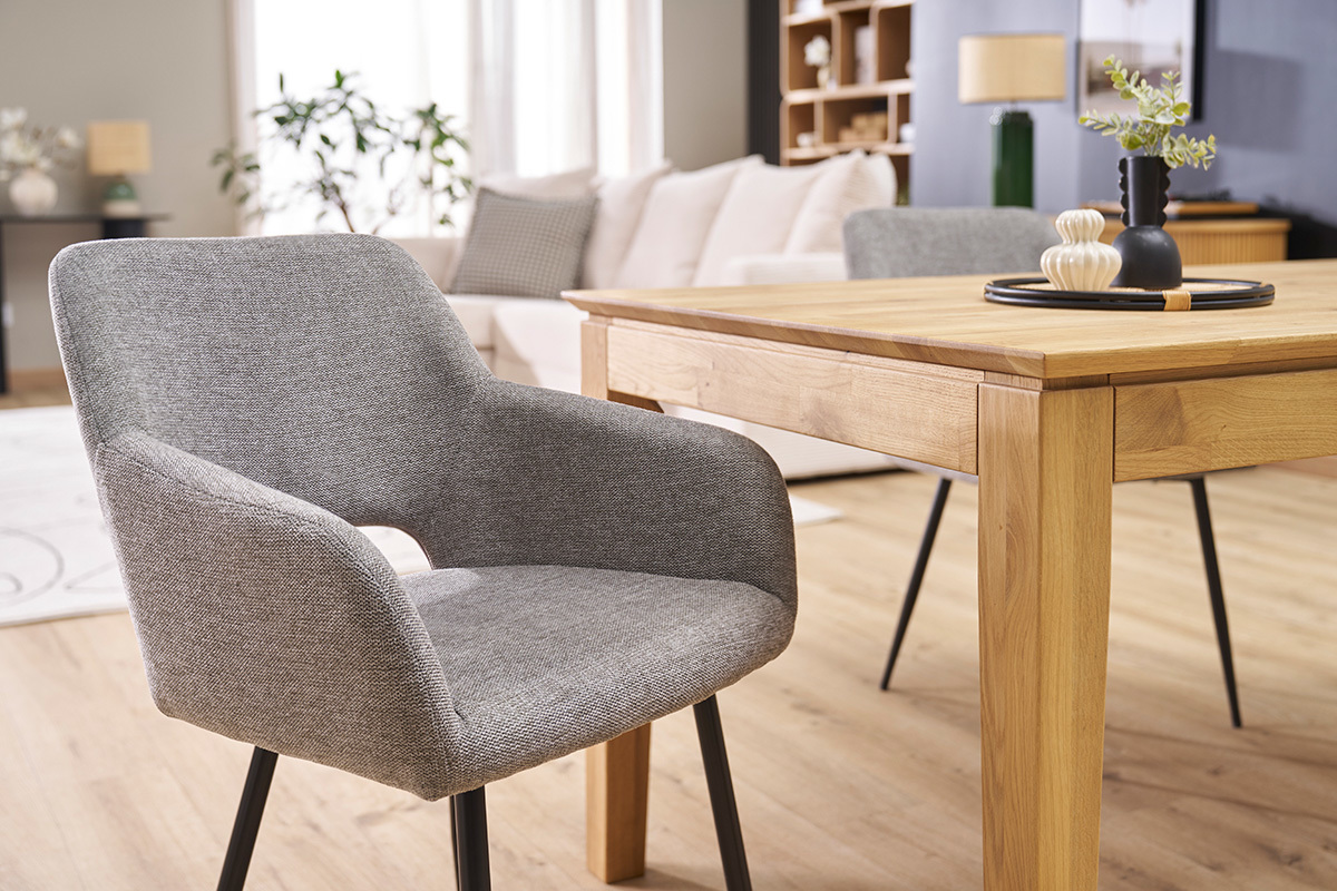 Stuhl aus grauem Samtstoff mit schwarzen Metallbeinen, 3/4 Ansicht in der N�he eines Holztisches.