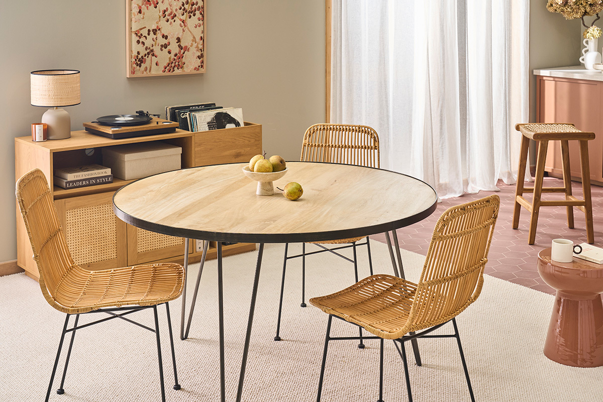 St�hle aus Rattan und schwarzem Metall um einen runden Holztisch.