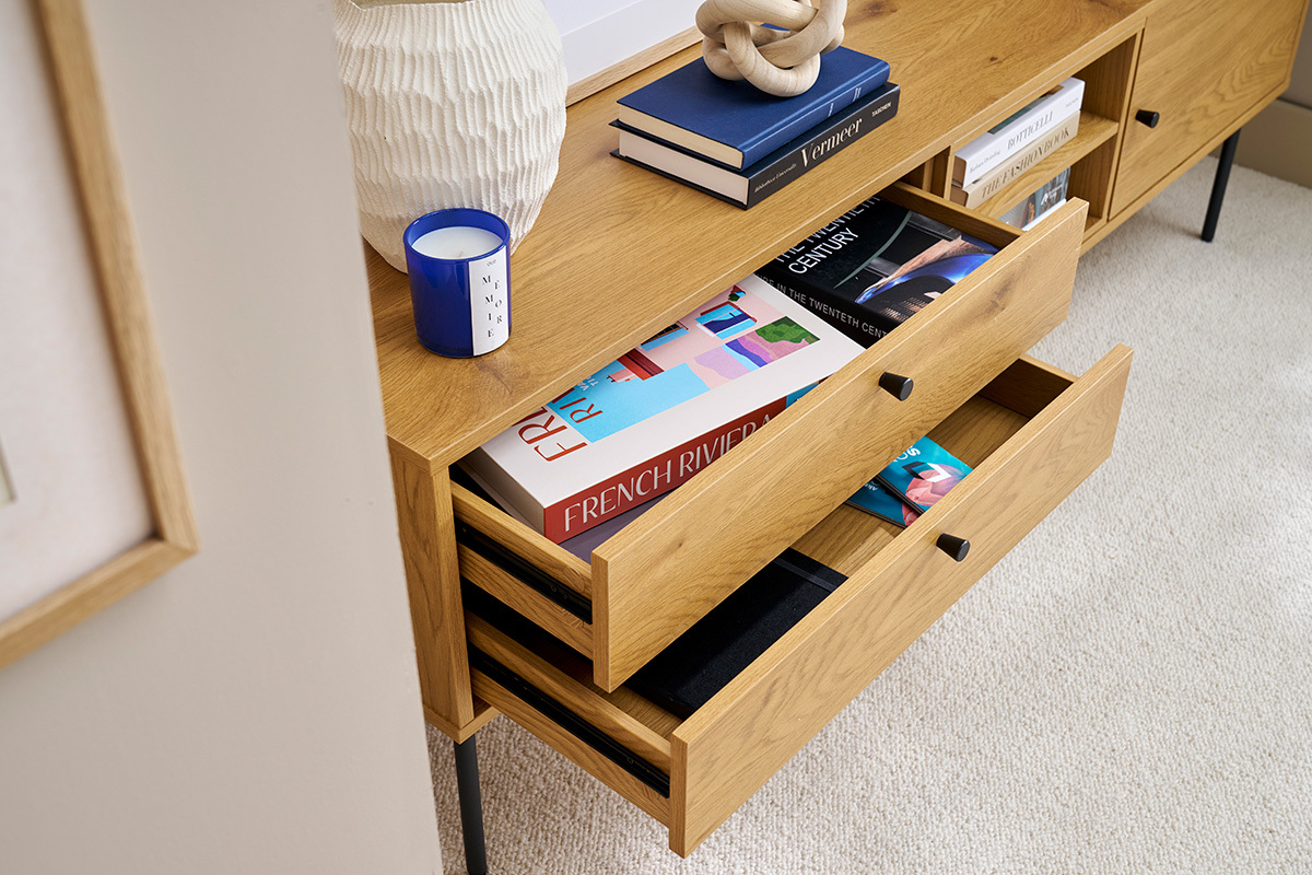 Helles Holzmbel fr Fernseher mit offenen Schubladen, Bchern und Deko-Objekten darauf.