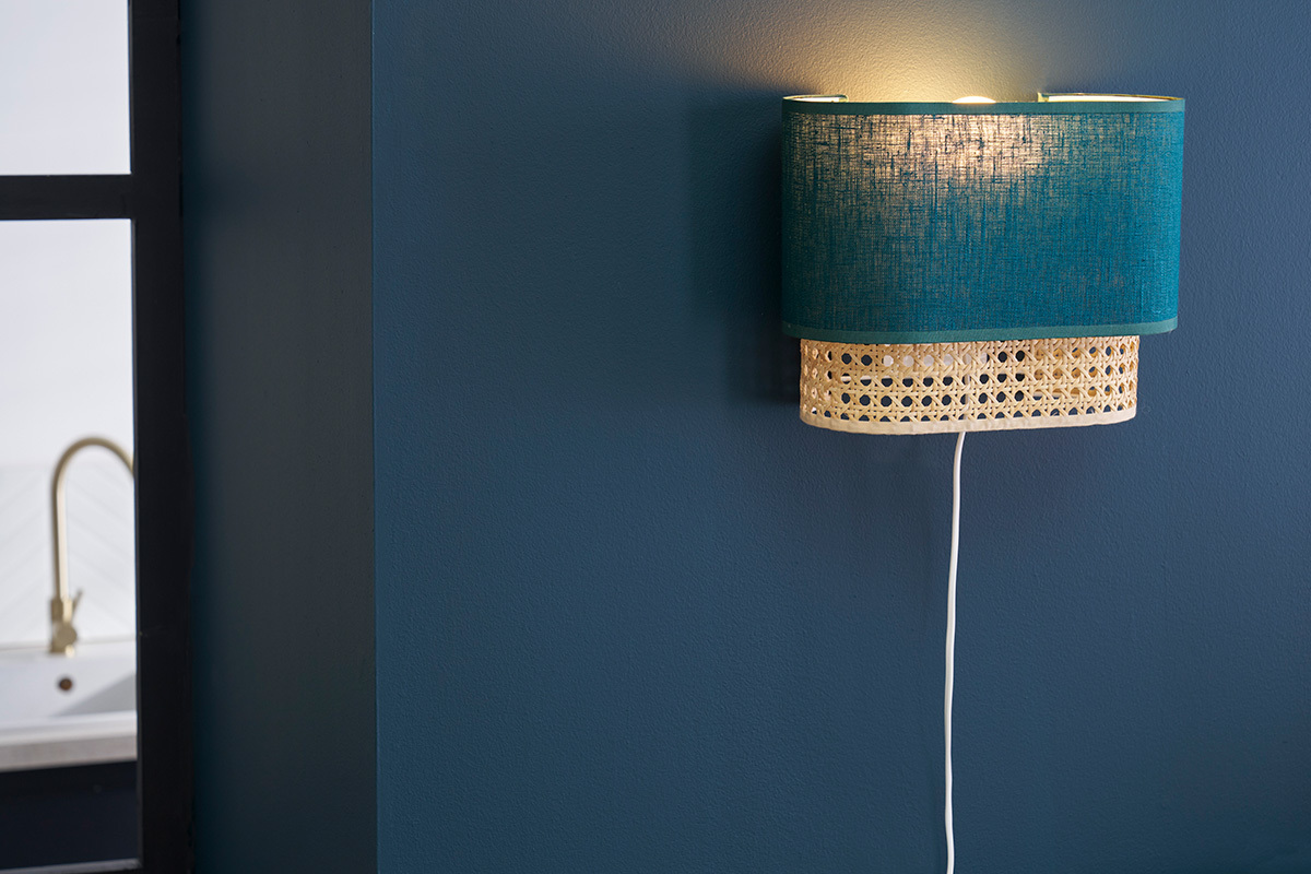 Wandleuchte in Entenblau und Rattan, Seitenansicht, an blauer Wand.